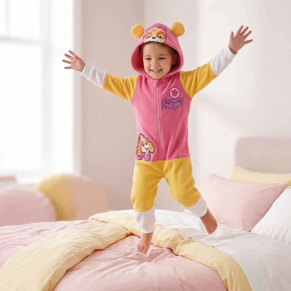 Meisje in Paw Patrol Skye onesie springt vrolijk op bed